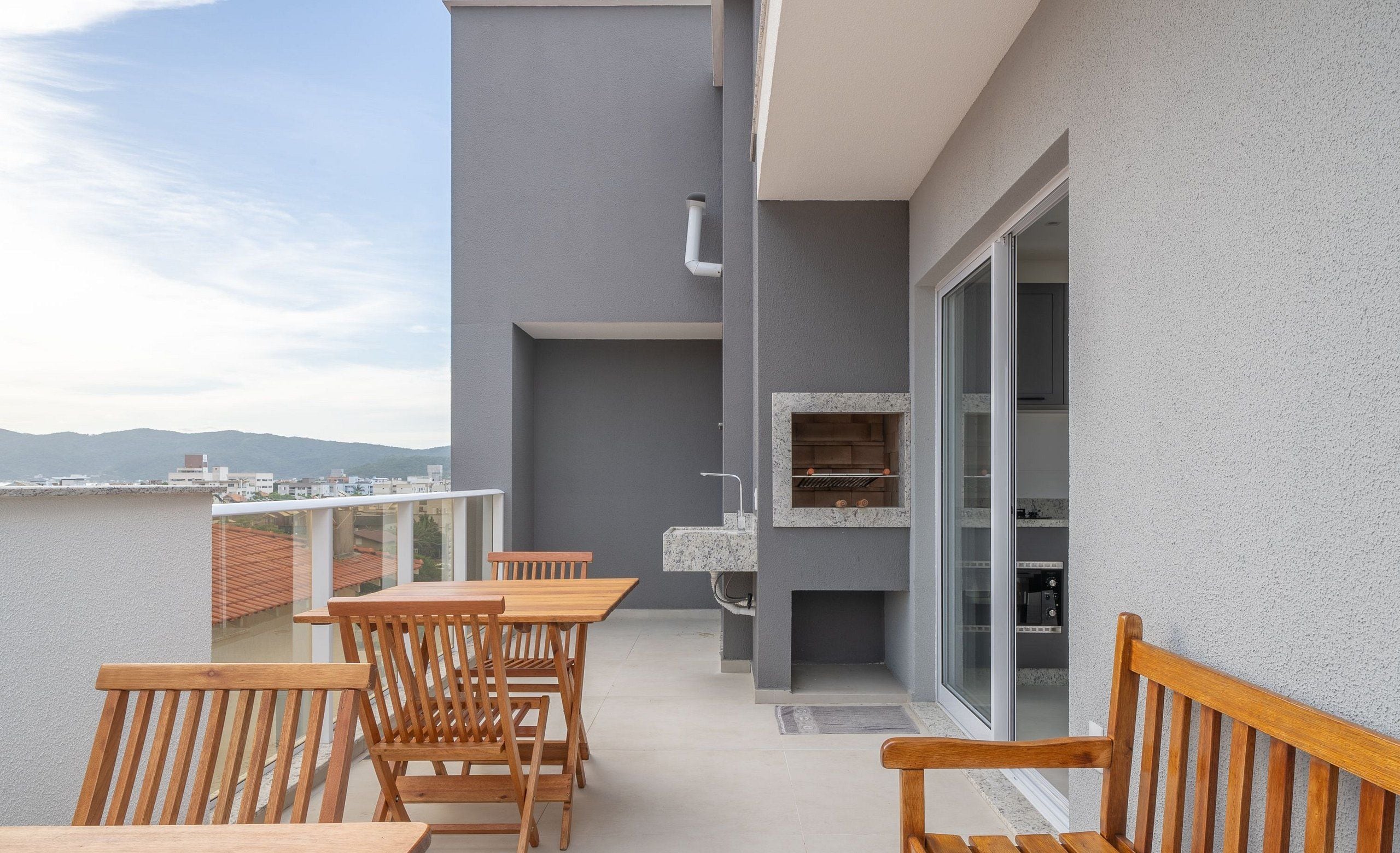 Un balcon doté de mobilier en bois, d’un barbecue intégré et offrant une vue sur la ville et les montagnes.