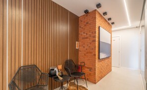 Een moderne kamer met een wand van houten latten, een accentmuur van baksteen, een wandgemonteerde televisie en twee zwarte stoelen met een klein tafeltje.