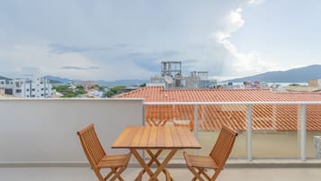 Terraço no telhado com mesa e cadeiras de madeira, com vista para uma paisagem urbana com edifícios e montanhas.