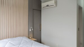 Een moderne slaapkamer met een bed, nachtkastje, wandairconditioner en een deur.