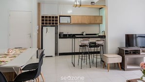 Een moderne keuken met een magnetron, spoelbak en houten keukenkastjes. Er is een eettafel met stoelen en een tv-meubel met een flatscreen televisie.