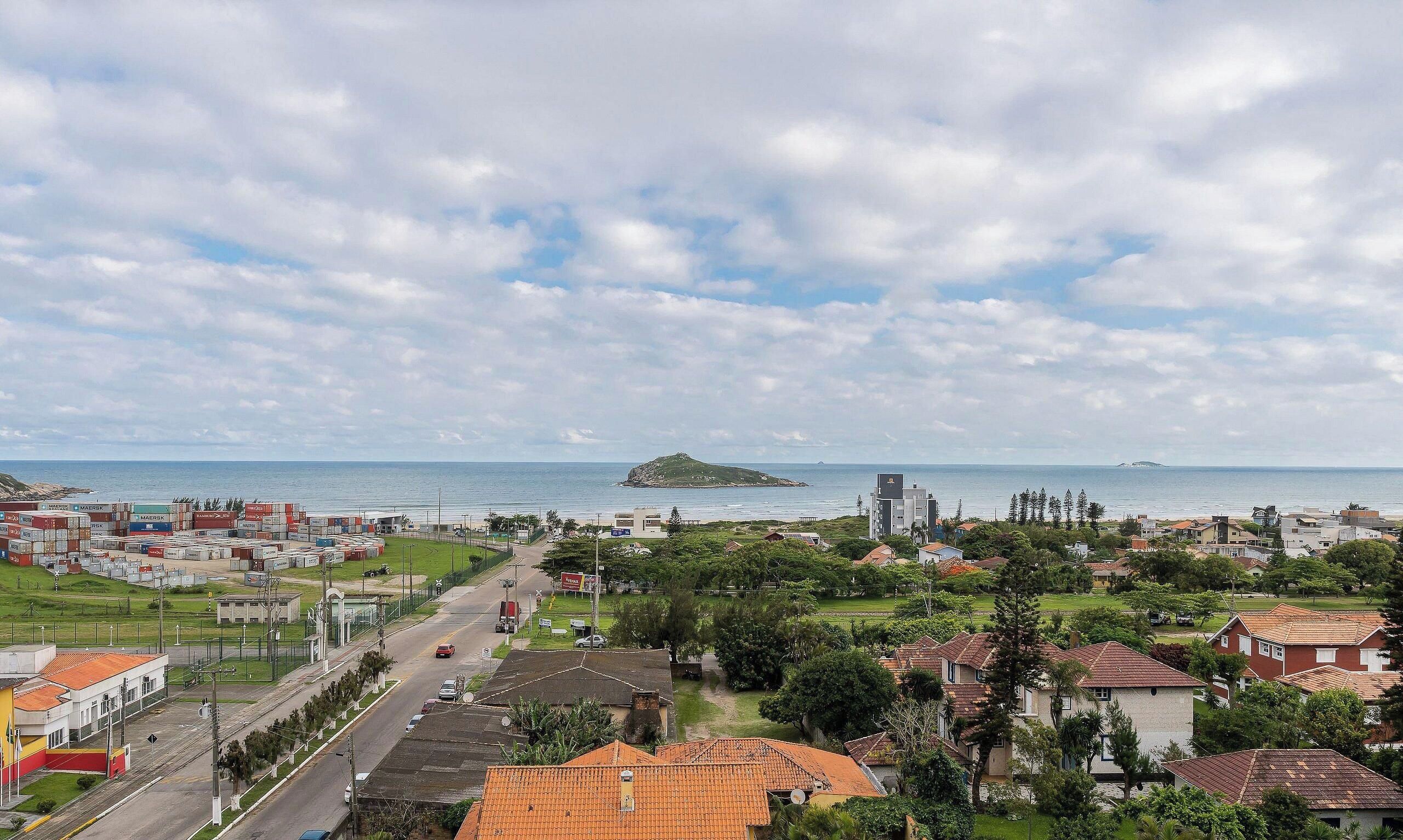 Uma cidade costeira com edifícios residenciais e comerciais, céu claro e vista para o mar.