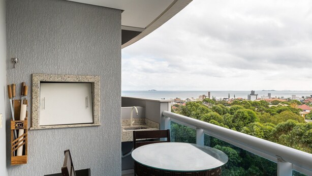 Een balkon met een ronde tafel en stoelen, een deur met een afbeelding, en uitzicht op een stadsbeeld en zee.