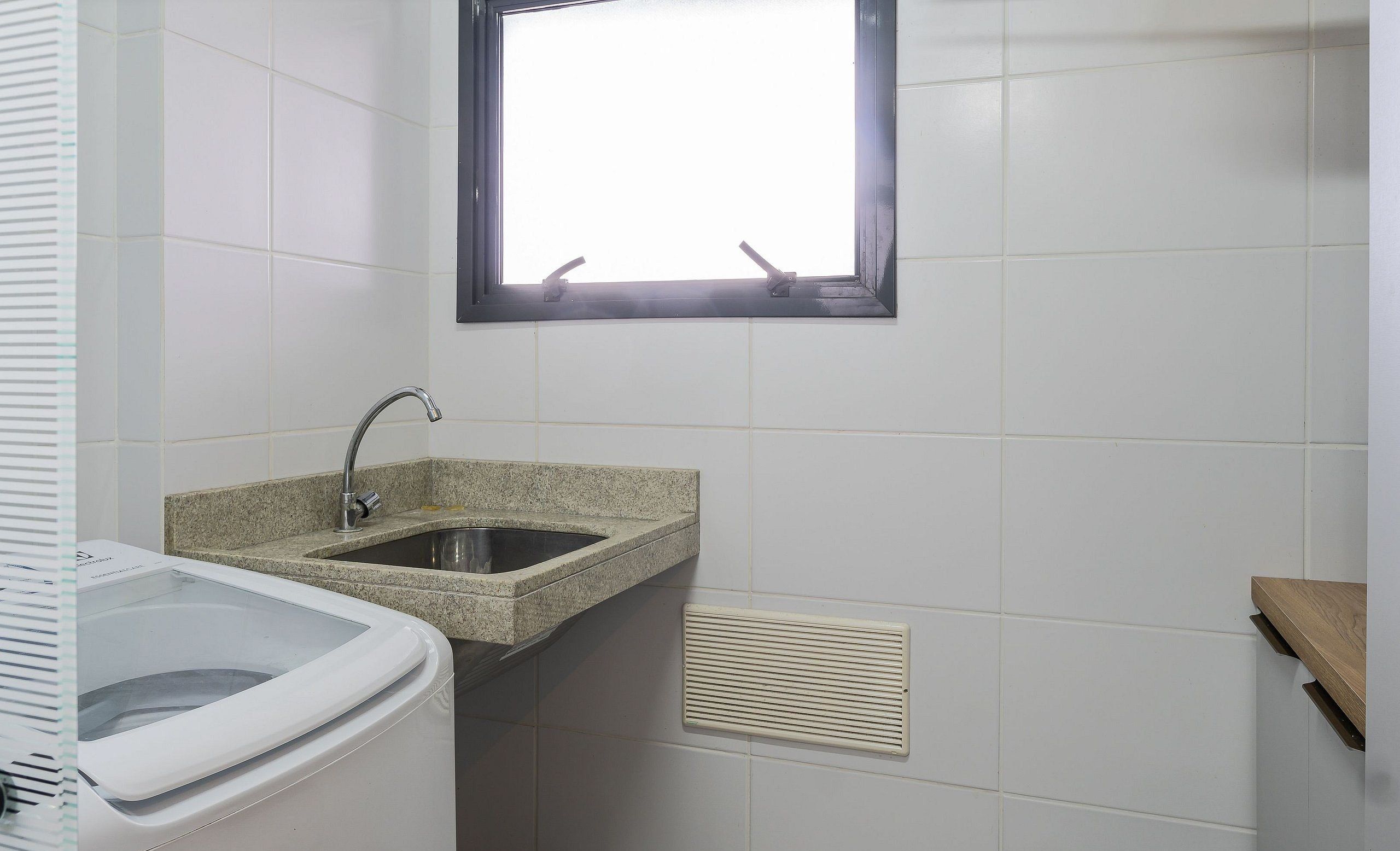 A small bathroom with a sink, a window, and a ventilation grille.