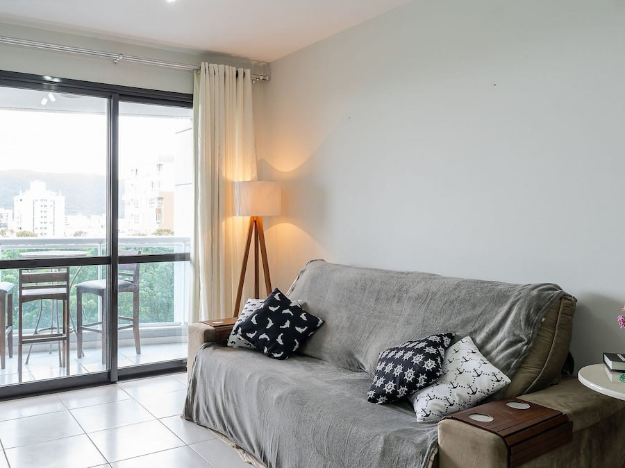 A living room with a grey sofa, a TV on a stand, a lamp, and a view of a balcony with chairs and a table.