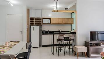 Een moderne keuken met een magnetron, spoelbak en houten keukenkastjes. Er is een eettafel met stoelen en een tv-meubel met een flatscreen televisie.