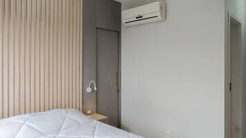 A modern bedroom with a bed, a bedside table, a wall-mounted air conditioner, and a door.