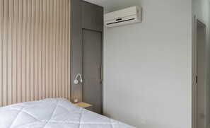 A modern bedroom with a bed, a bedside table, a wall-mounted air conditioner, and a door. - Apt W/balcony and BBQ 500m From the Beach Rml605 (Imbituba)