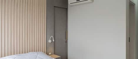 A modern bedroom with a bed, a bedside table, a wall-mounted air conditioner, and a door.