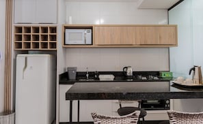 A modern kitchen with a built-in microwave, a coffee maker, and a kettle. There is a refrigerator, a sink, and a dining area with two chairs. - Apt W/balcony and BBQ 500m From the Beach Rml605 (Imbituba)