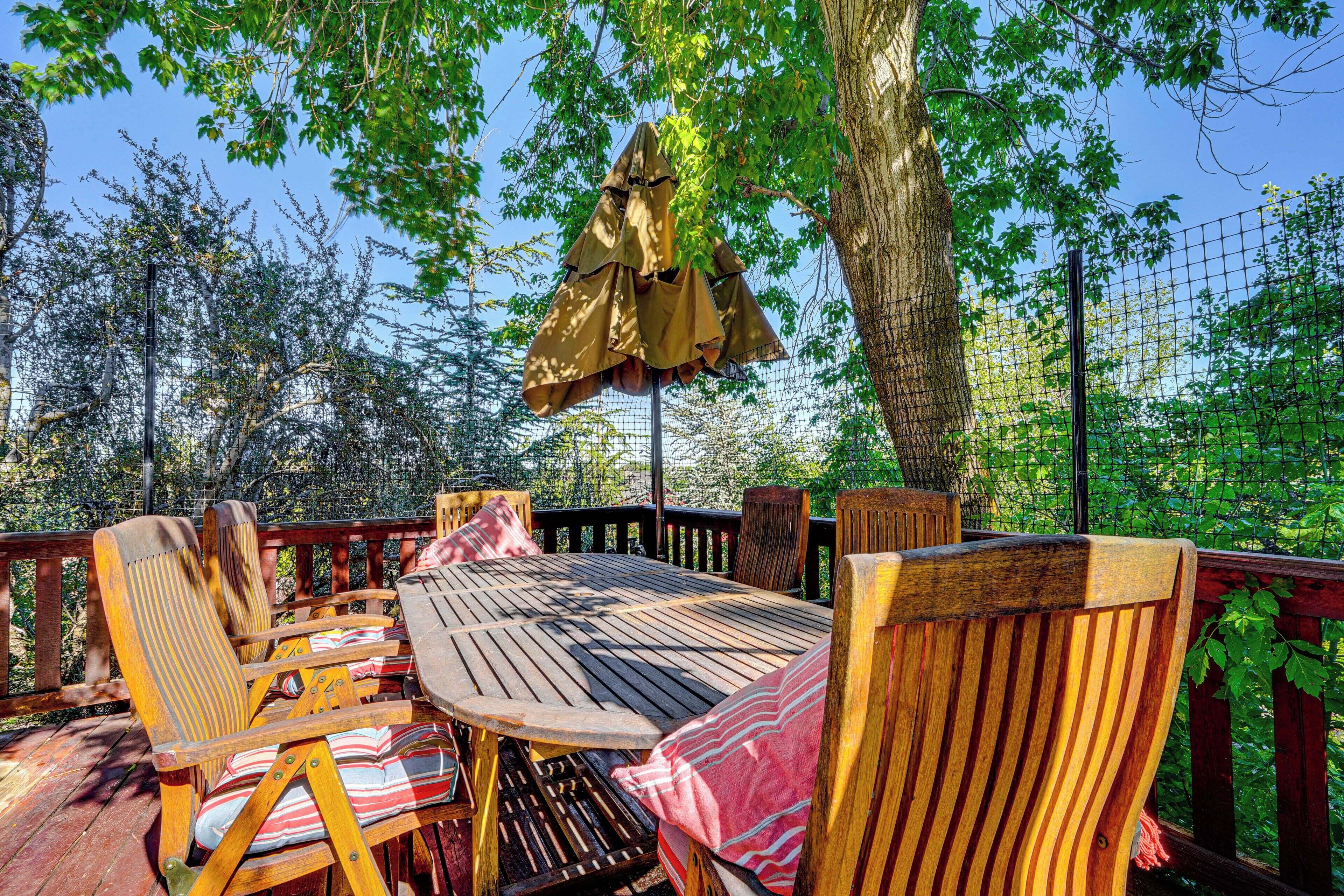 Une terrasse extérieure en bois, avec une table ronde et des chaises, entourée d’une clôture en bois et d’arbres.