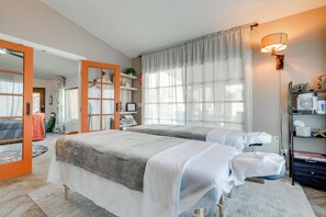Ein Hotelzimmer mit zwei Betten, einem großen Fenster mit Vorhängen, einem Bücherregal und einem Kleiderschrank mit Spiegel.