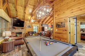 A wooden interior with a pool table, leather sofa, and a fireplace.