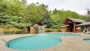 A pool area with a waterfall feature, stone flooring, and wooden cabins. - 1 Mi to Dtwn Gatlinburg: Hot Tub Haven in Smokies! (Gatlinburg)