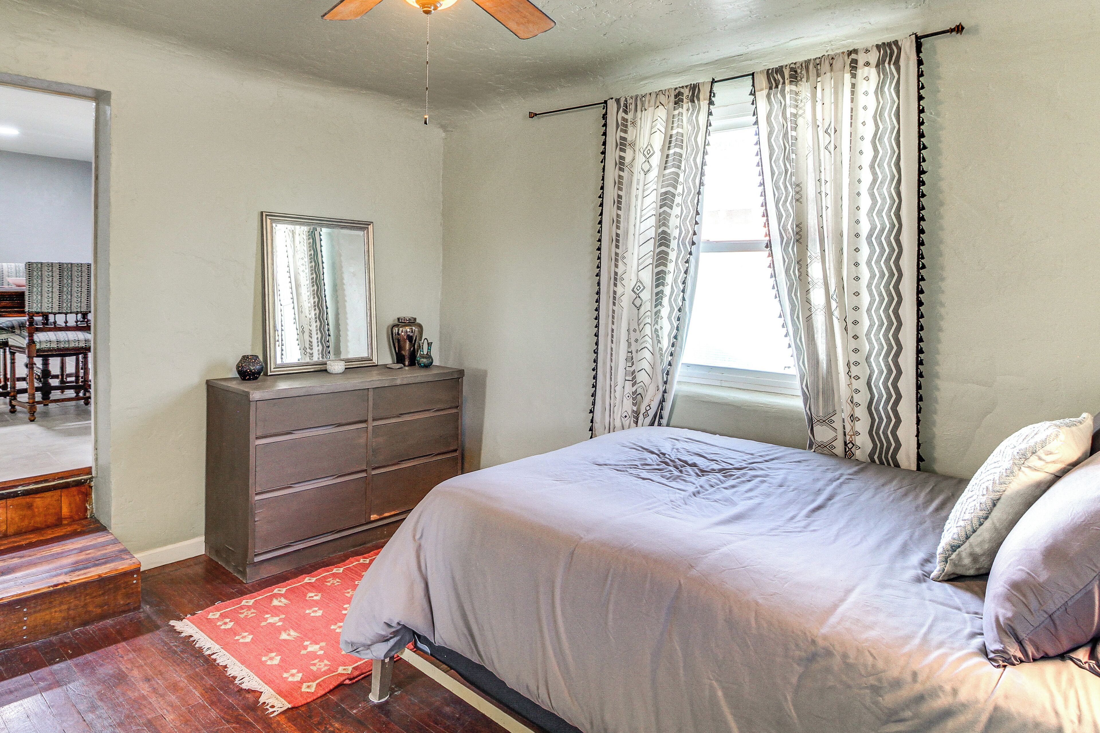 A bedroom with a bed, a dresser, a mirror, and a window with curtains.
