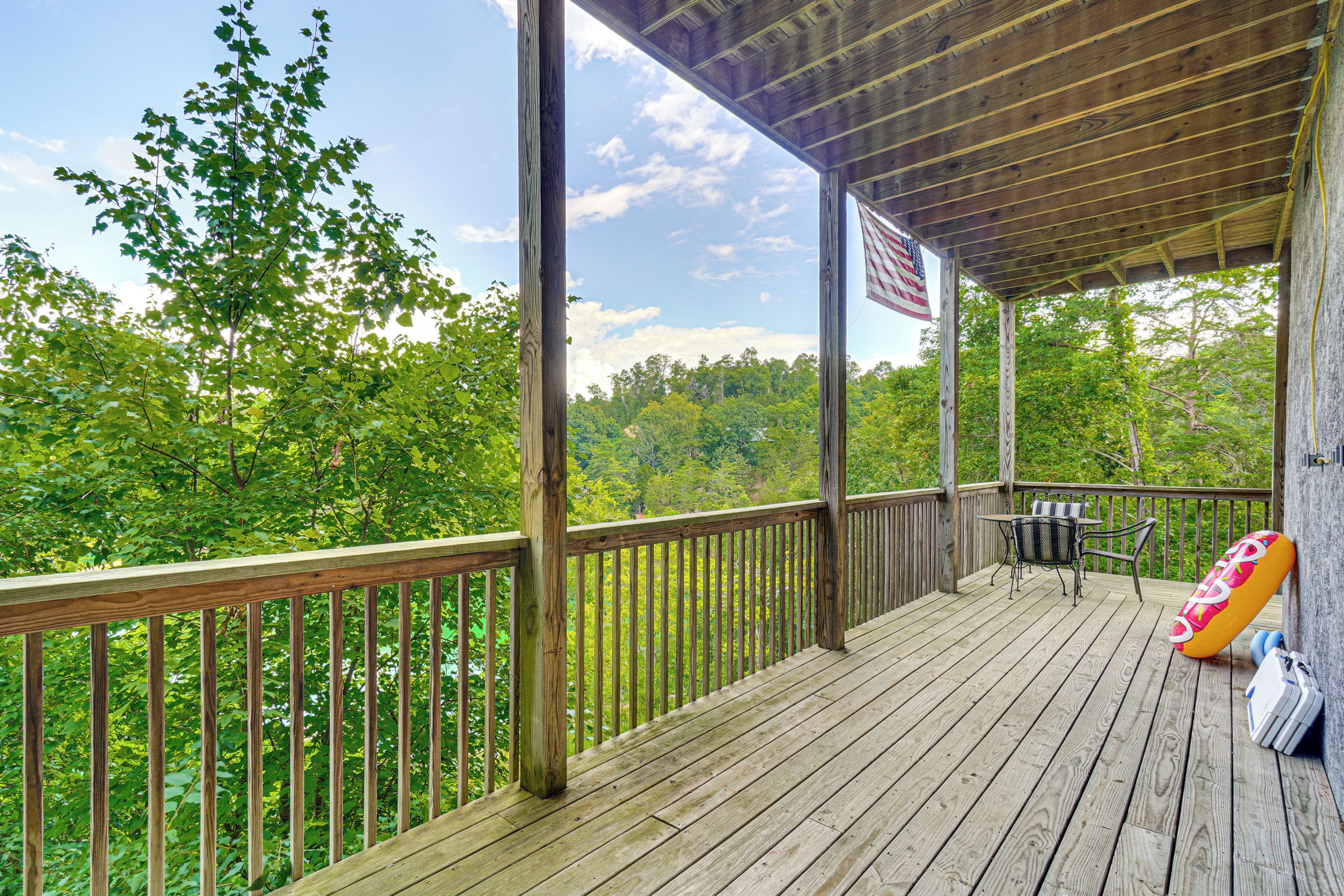 A wooden deck with a view of a forest, an American flag, and outdoor furniture.