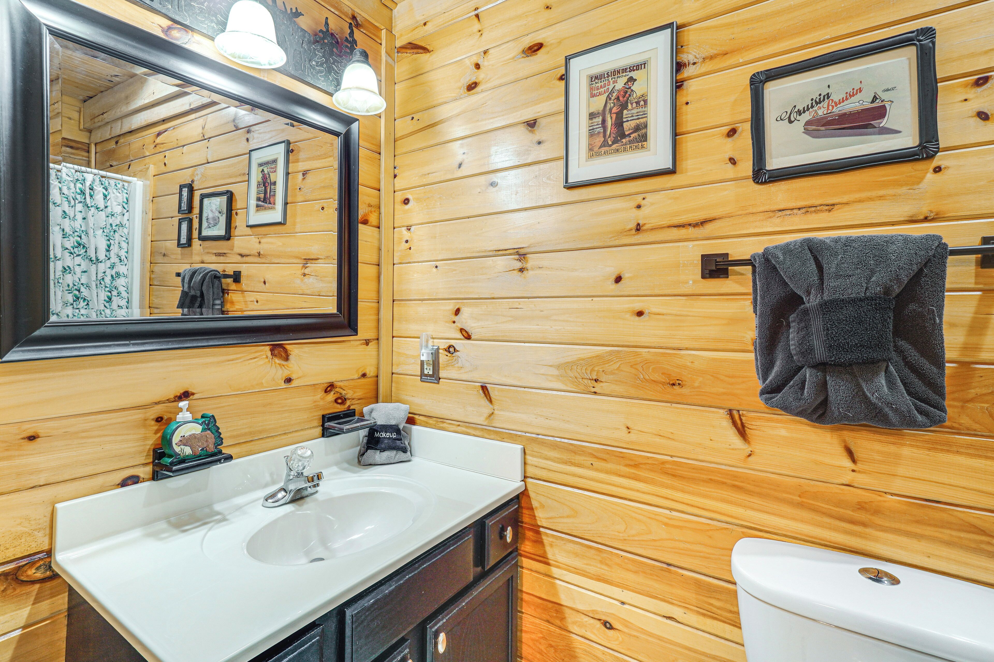 Ein Badezimmer mit Holzwänden, einem Waschbecken, einem Spiegel, einem Handtuchhalter und gerahmten Bildern an der Wand.