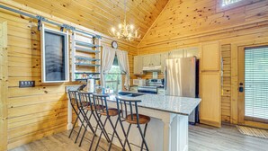 A wooden cabin kitchen with a central island, bar stools, a chandelier, and a refrigerator. - Douglas Lake Access: Family Cabin in Sevierville! (Sevierville)