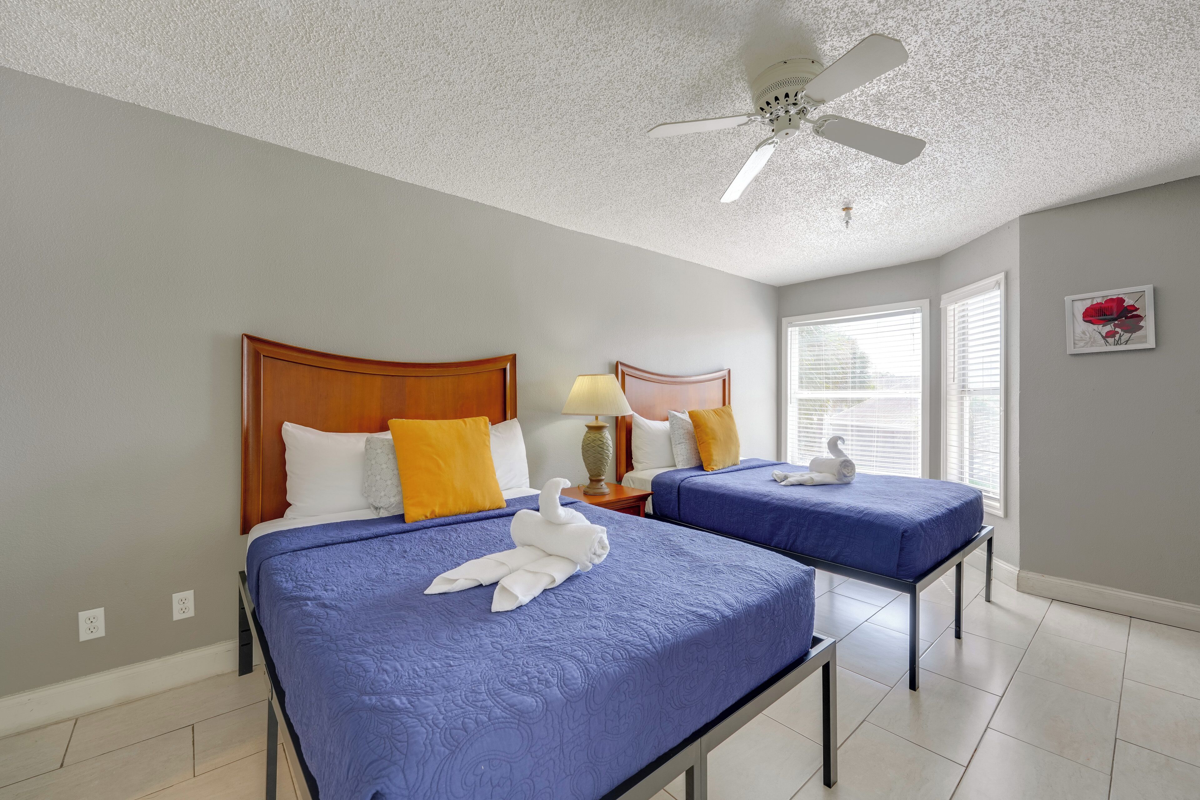 Quarto de hotel com duas camas, um ventilador de teto e uma janela com persianas.