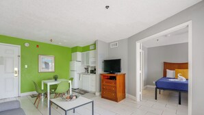 Ett kompakt bostadsutrymme med en matplats, ett litet kök och ett sovrum med en säng och en tv.