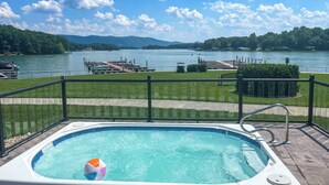 Ein Whirlpool mit Blick auf einen See und Boote, umgeben von einer Terrasse und einem Zaun.