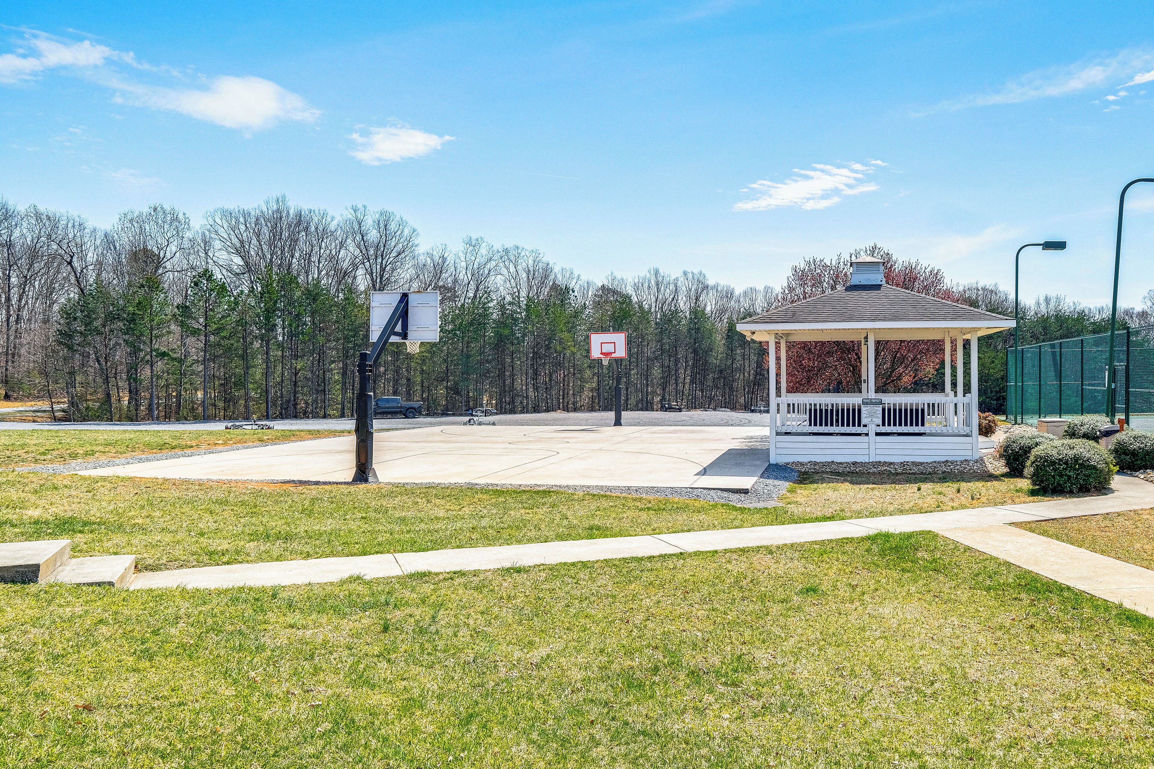 A gazebo with a basketball court in front, surrounded by trees and a clear sky.