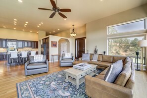 A spacious living room with a sofa, armchairs, and a coffee table. There is a kitchen area with a dining set and a ceiling fan.