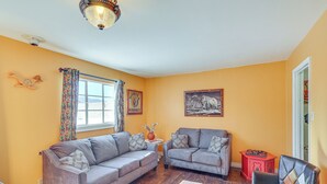 A living room with two grey sofas, a red side table, a wooden floor, and a window with curtains.