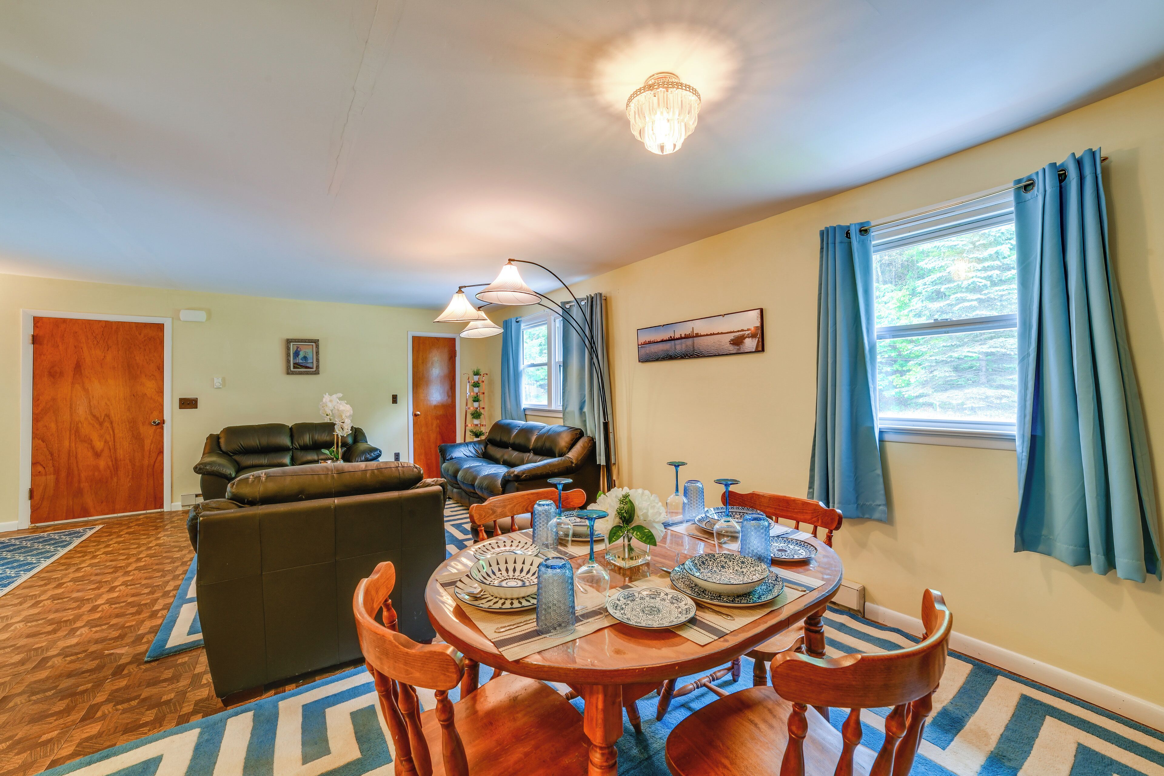 A dining area with a wooden table set for four, surrounded by wooden chairs. There is a brown leather sofa and a dining table with blue and white patterned tableware.