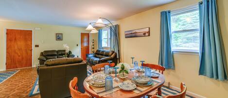 A dining area with a wooden table set for four, surrounded by wooden chairs. There is a brown leather sofa and a dining table with blue and white patterned tableware.