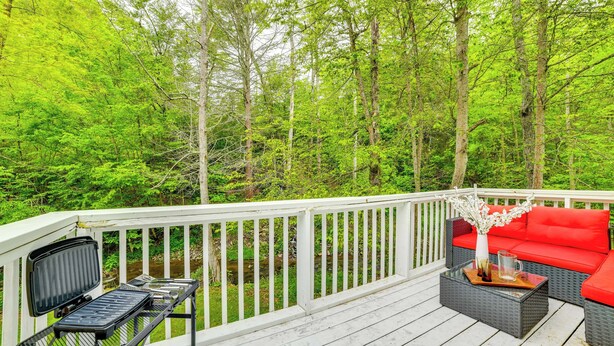 Eine Terrasse mit Gartenmöbeln, einem Grill und Blick auf einen Wald.