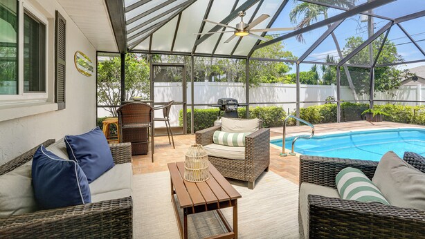 Uma área externa coberta com móveis de vime, piscina e ventilador de teto.