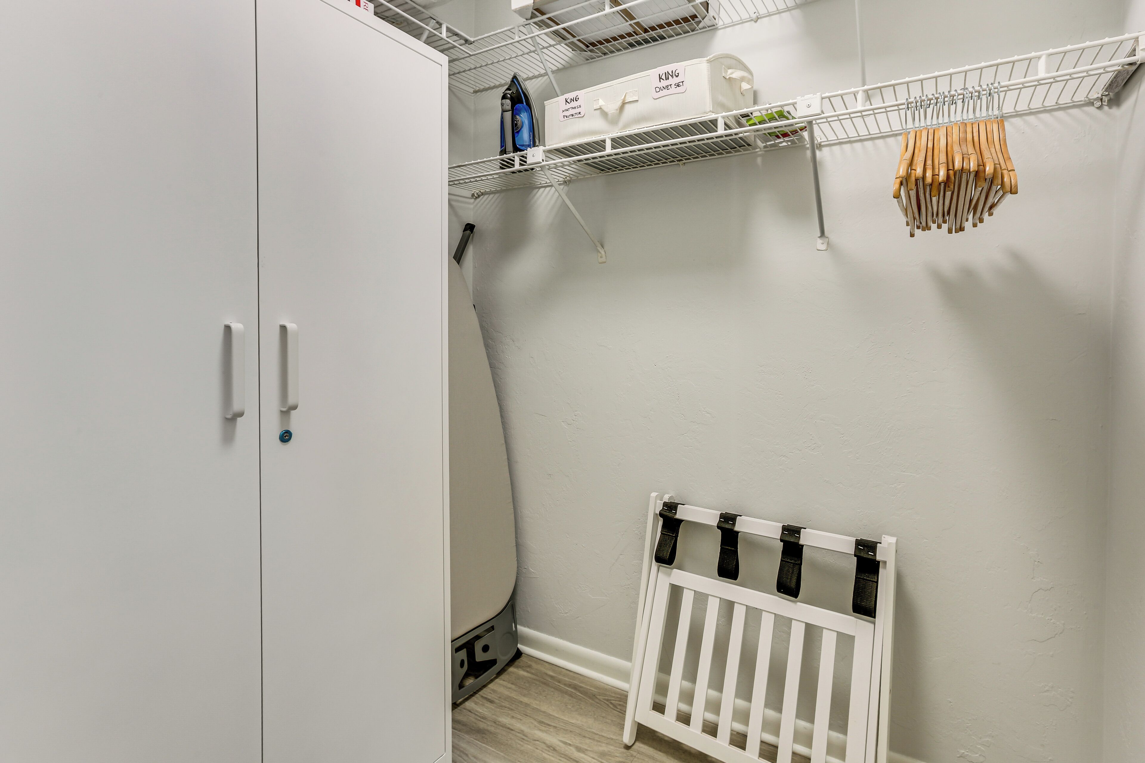 A laundry area with a white cabinet, a drying rack, and a shelf with ironing supplies.