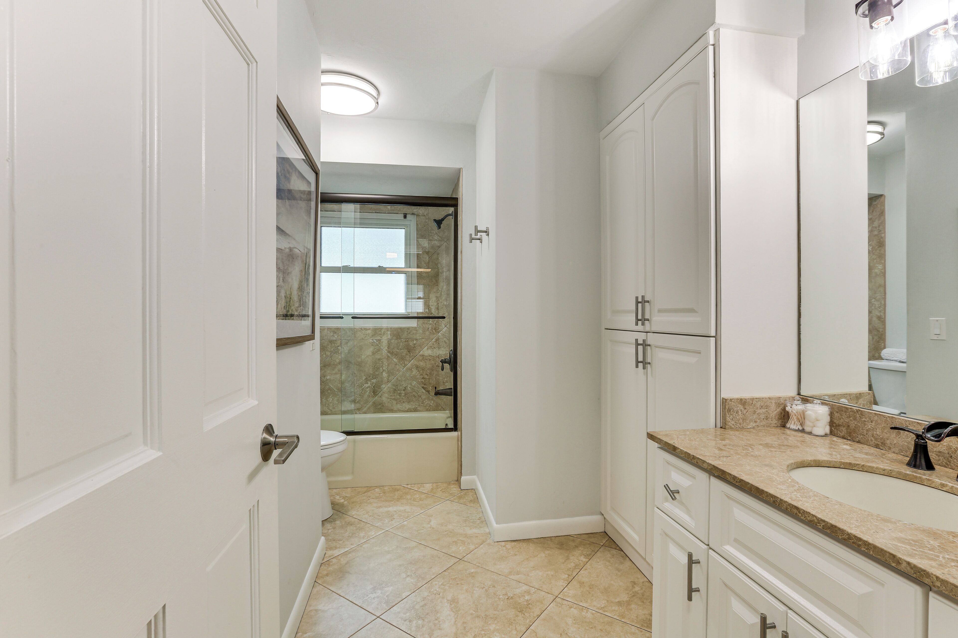 A modern bathroom with a glass shower enclosure, a large mirror, and a beige tiled floor.
