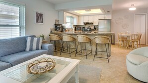 Uma cozinha moderna com banquetas, uma mesa de jantar e uma sala de estar com sofá e mesa de centro.