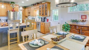 A spacious kitchen with wooden cabinets, a stainless steel refrigerator, and a dining area set with a table, chairs, and a chandelier. - Golf, Hike & Explore: Blue Ridge Mtn Haven w/ Deck (Roaring Gap)