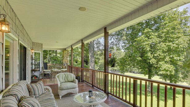 A covered porch with a wooden deck, a wicker sofa, a glass coffee table, and a view of a green lawn and trees. - Golf, Hike & Explore: Blue Ridge Mtn Haven w/ Deck (Roaring Gap)