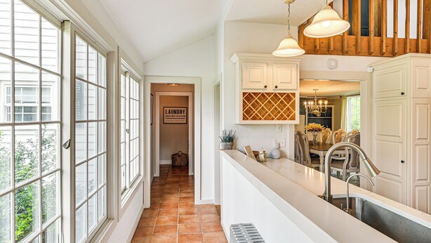 A spacious kitchen with a large window, a built-in sink, and a dining area visible in the background.