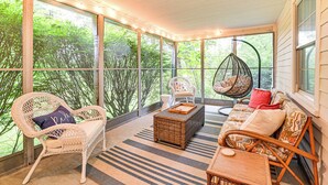 A covered porch with wicker furniture, a hanging chair, and a view of greenery.