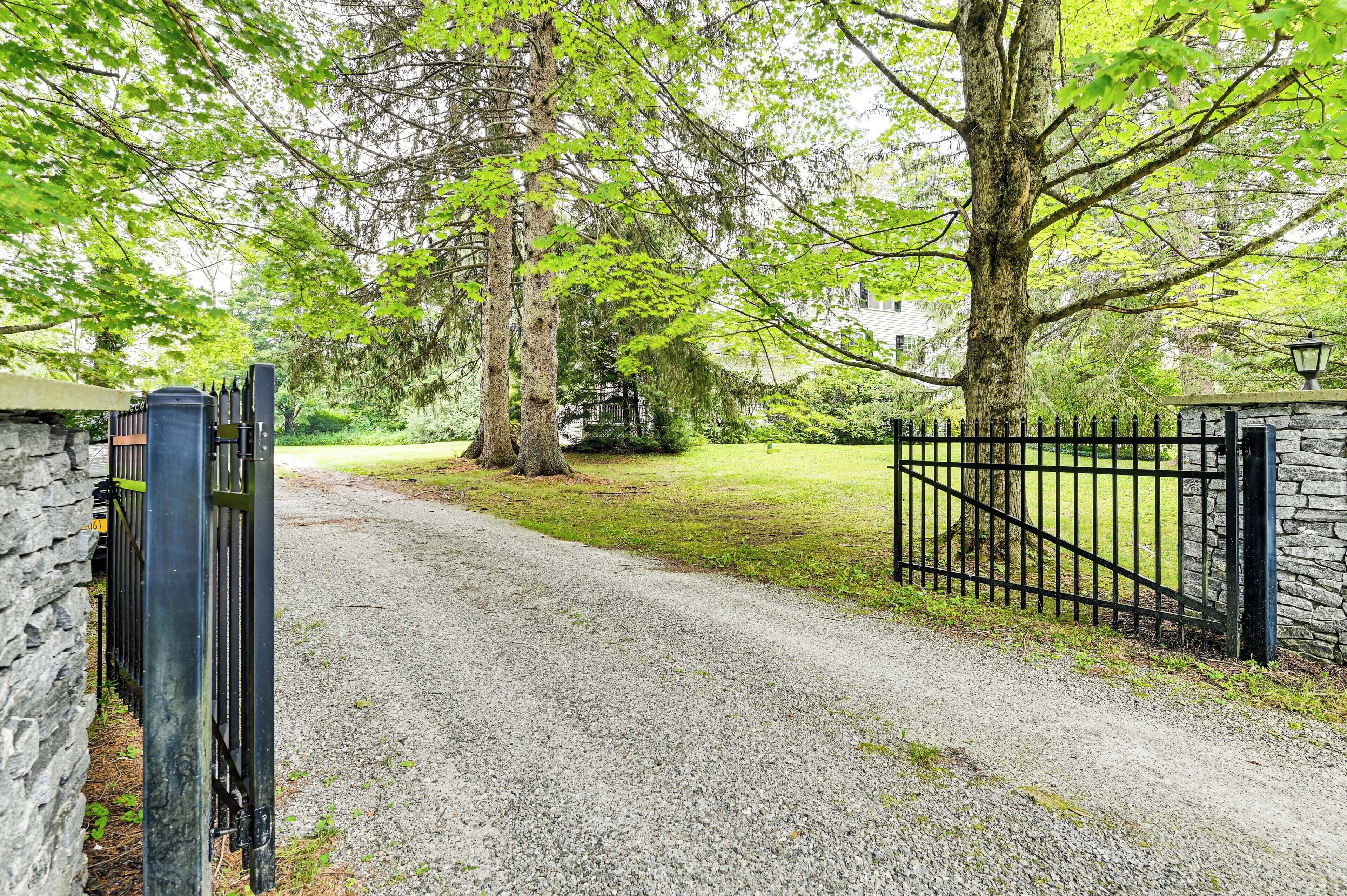 A gravel driveway leading to a gated entrance with a stone wall and a metal gate.