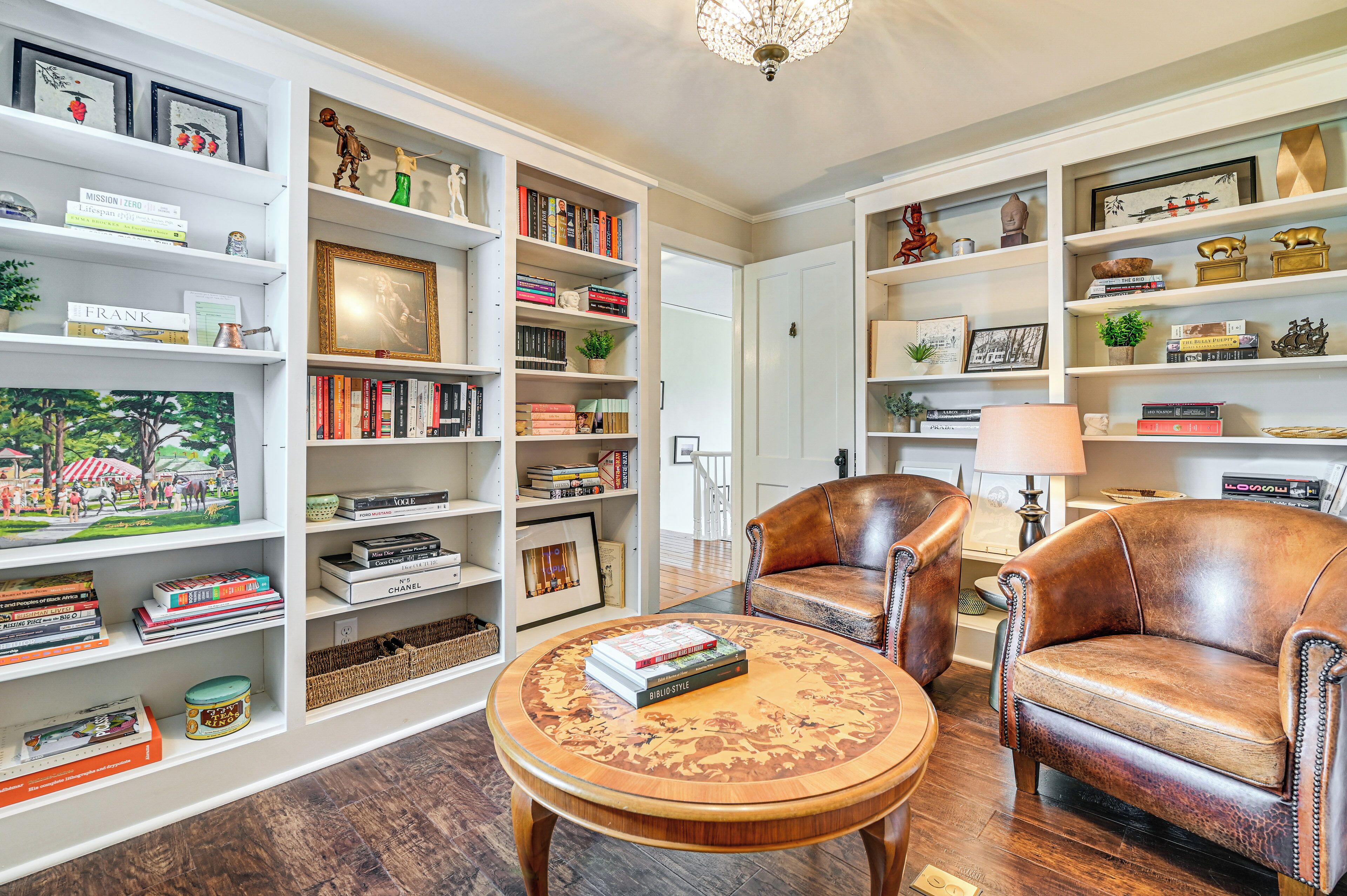Un salón bien organizado con un sofá de cuero, una mesa de centro con libros y una estantería llena de libros y objetos decorativos.