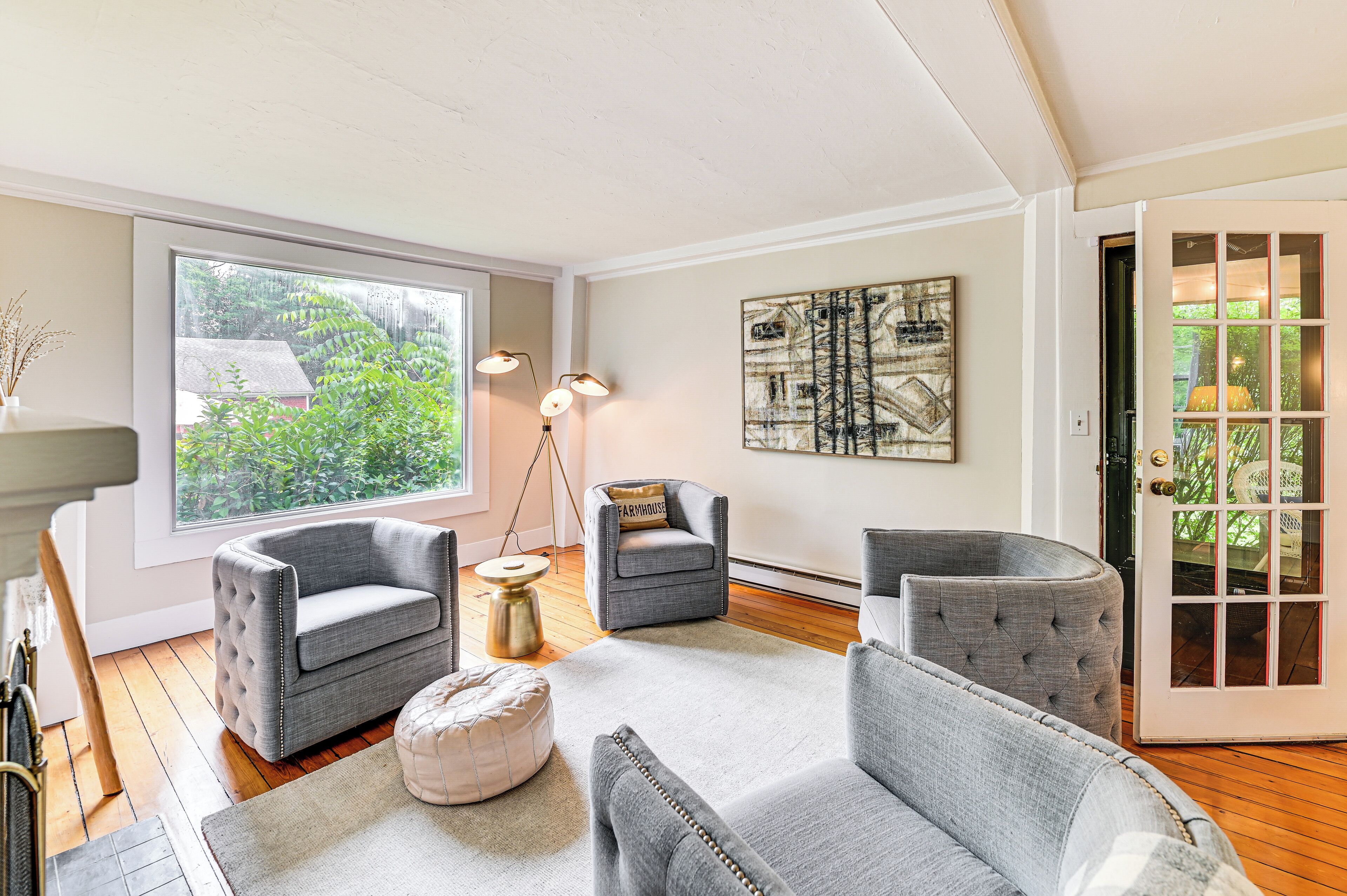 A living room with a large window, a gray sofa, a chair, a lamp, and a painting on the wall.