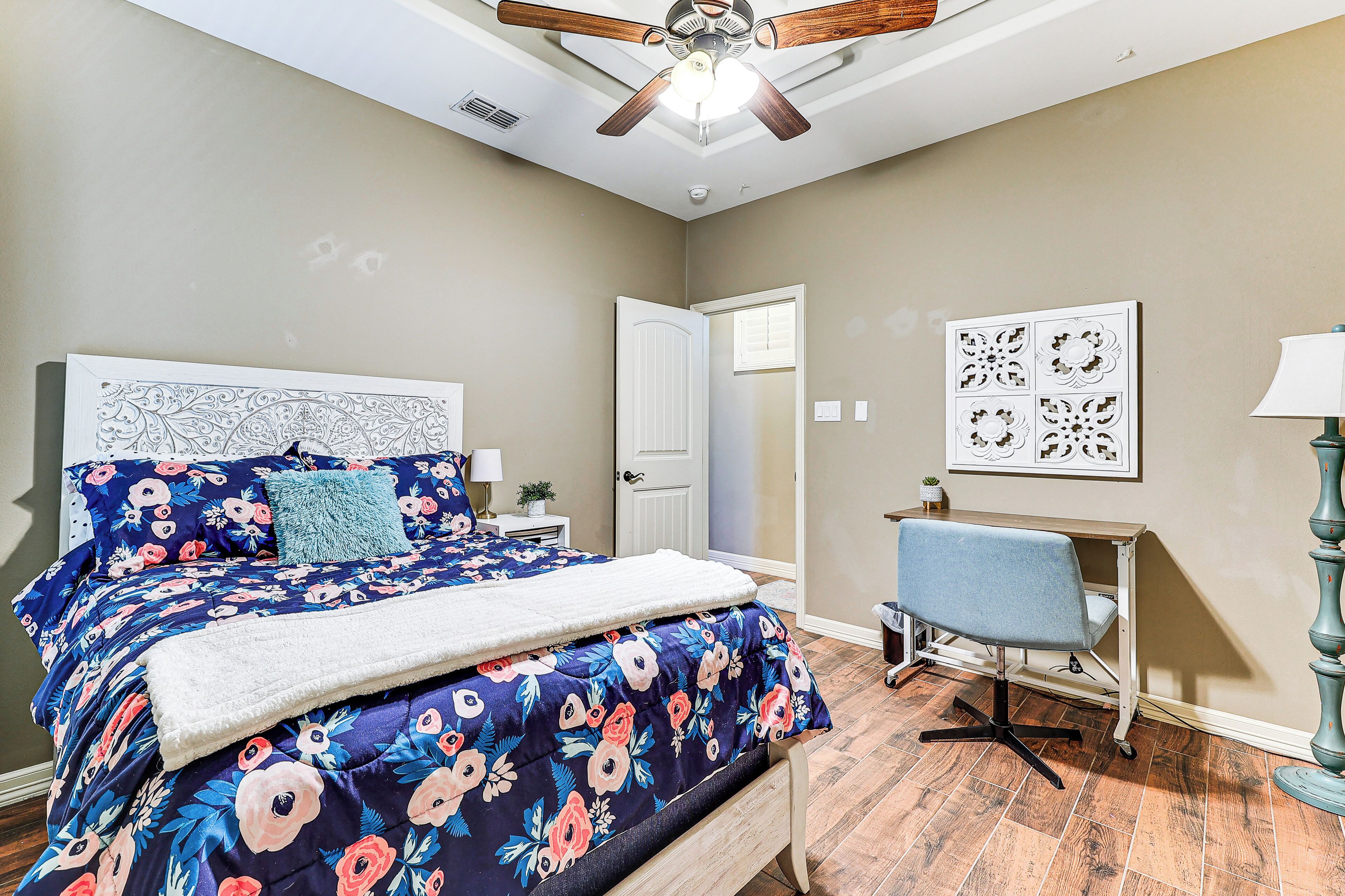 A bedroom with a bed, a desk, a chair, and a ceiling fan.