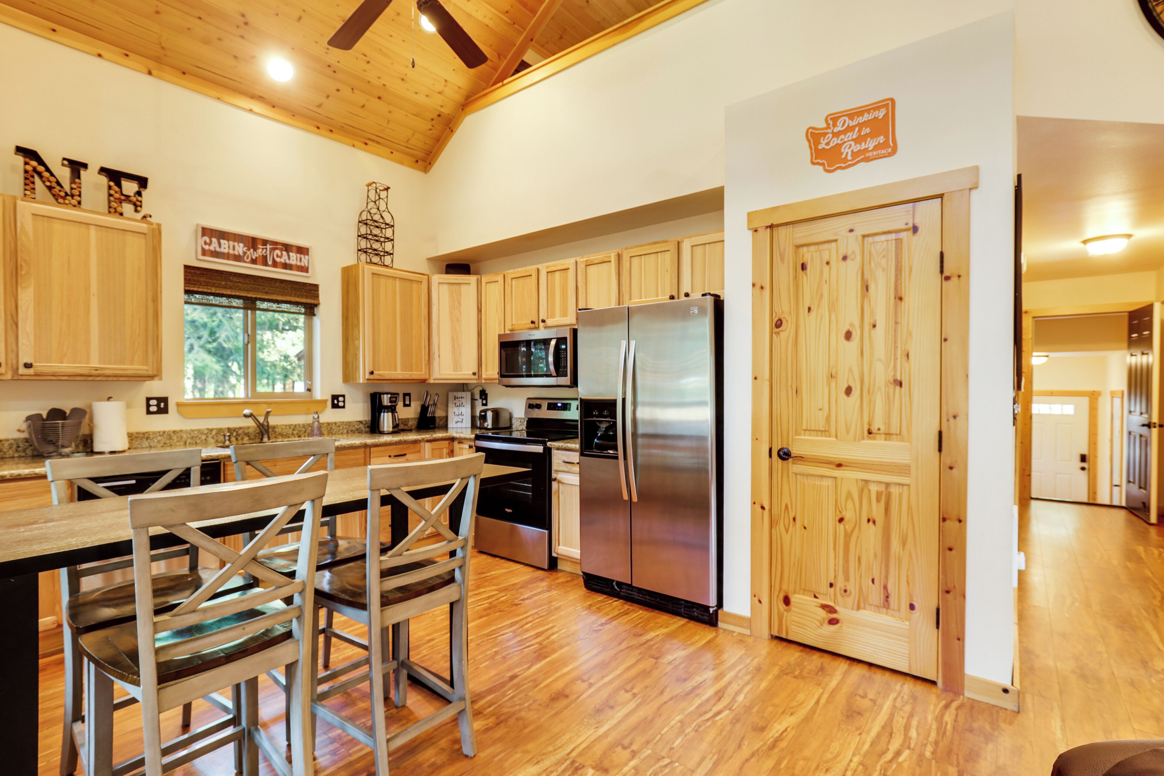 A modern kitchen with wooden cabinets, stainless steel appliances, and a dining area with bar stools.