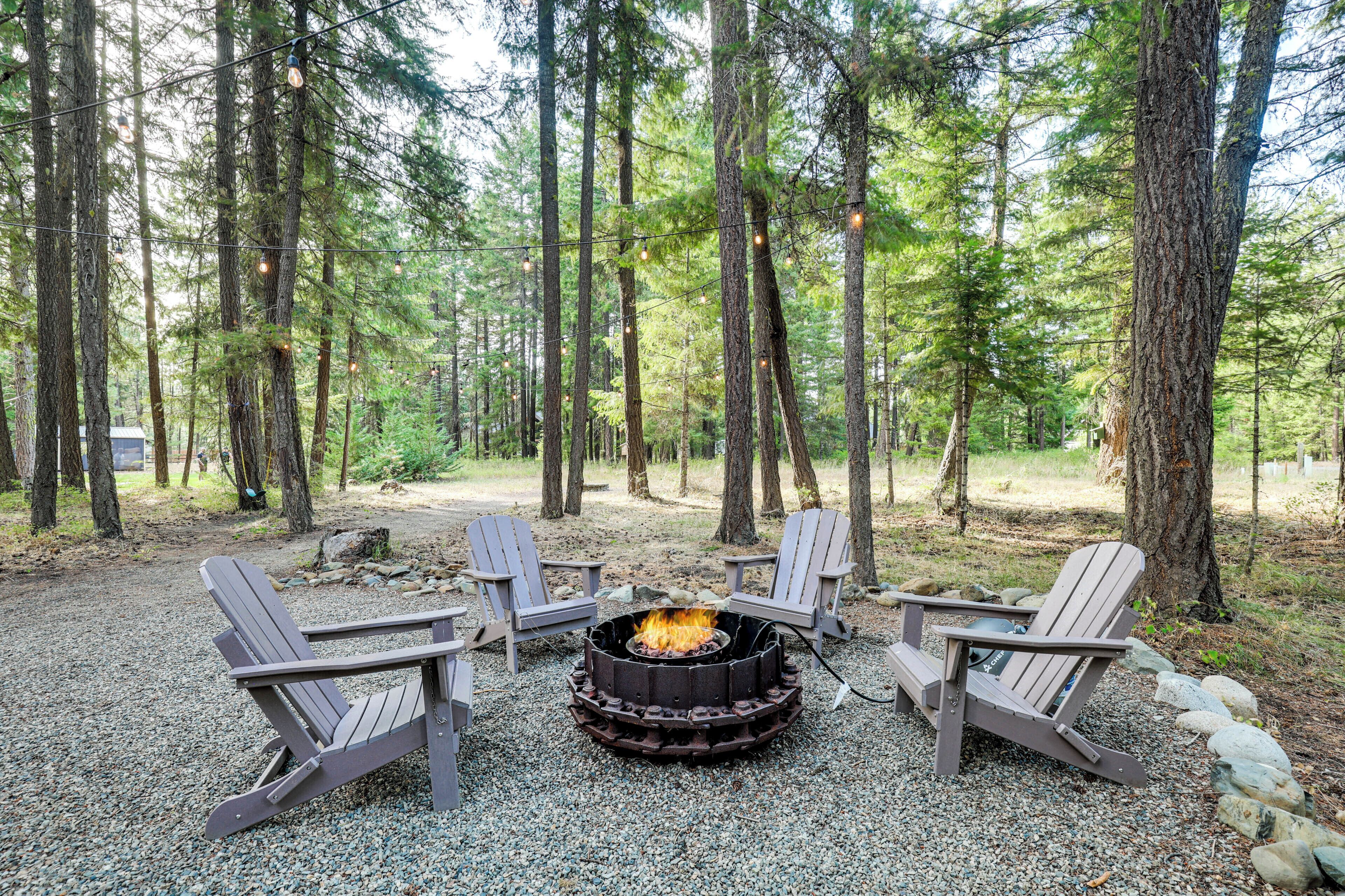 Een kampeerterrein omgeven door bos, met een vuurkuil en Adirondack-stoelen.