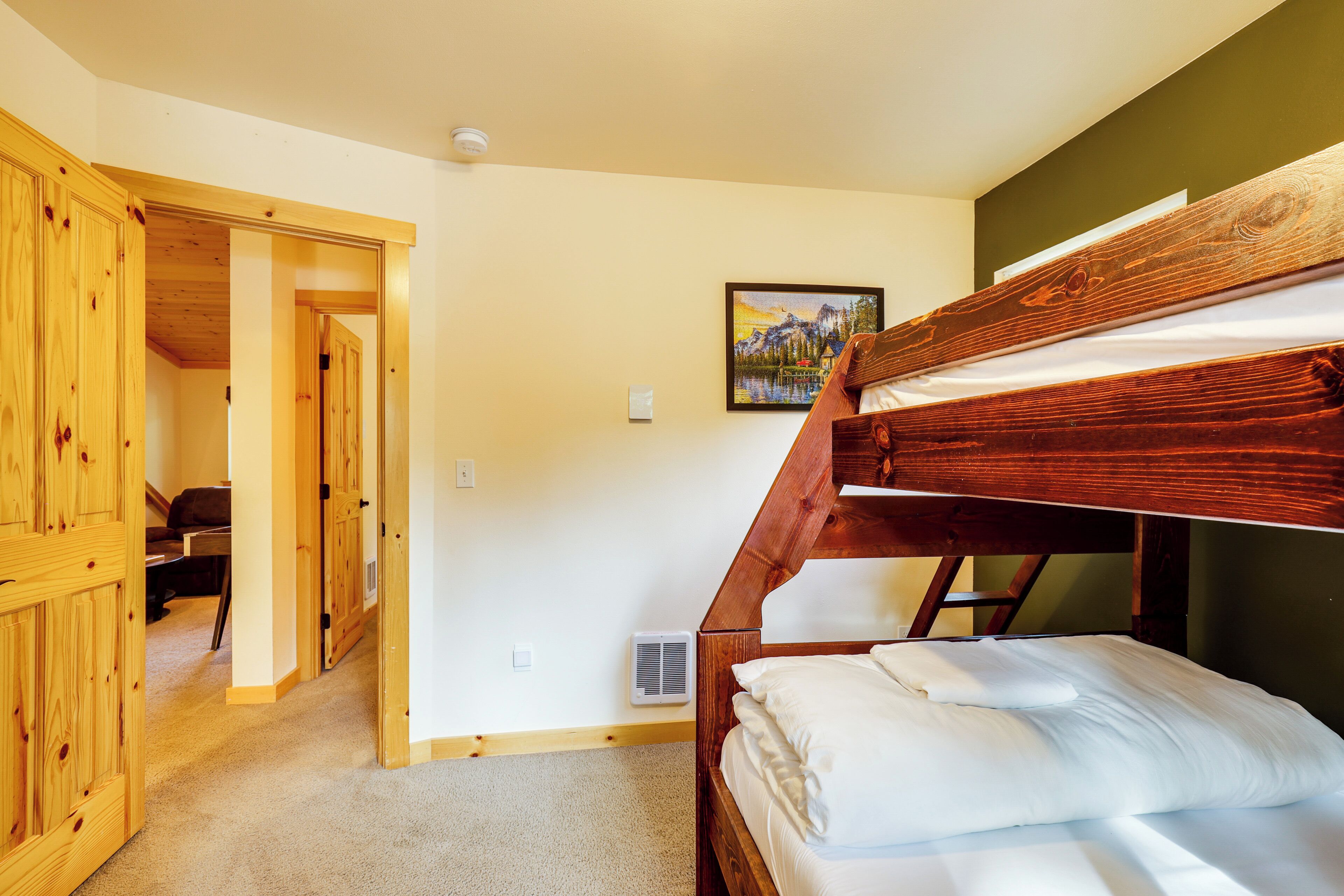 Une chambre avec un lit superposé doté d’une tête de lit en bois, une porte donnant sur une autre pièce et un tableau encadré accroché au mur.