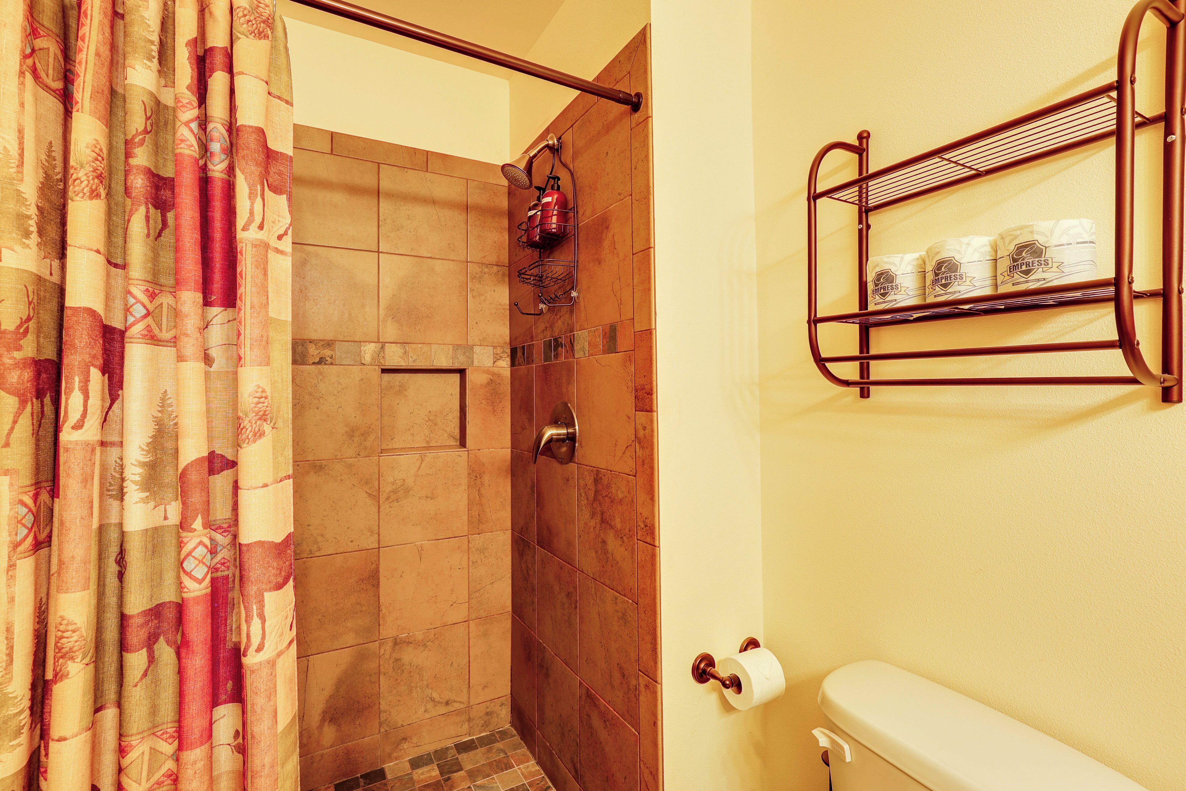 A bathroom with a shower, a toilet, and a shelf with toiletries.