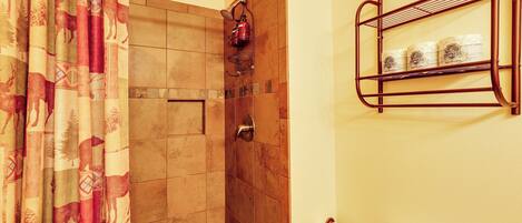 A bathroom with a shower, a toilet, and a shelf with toiletries.