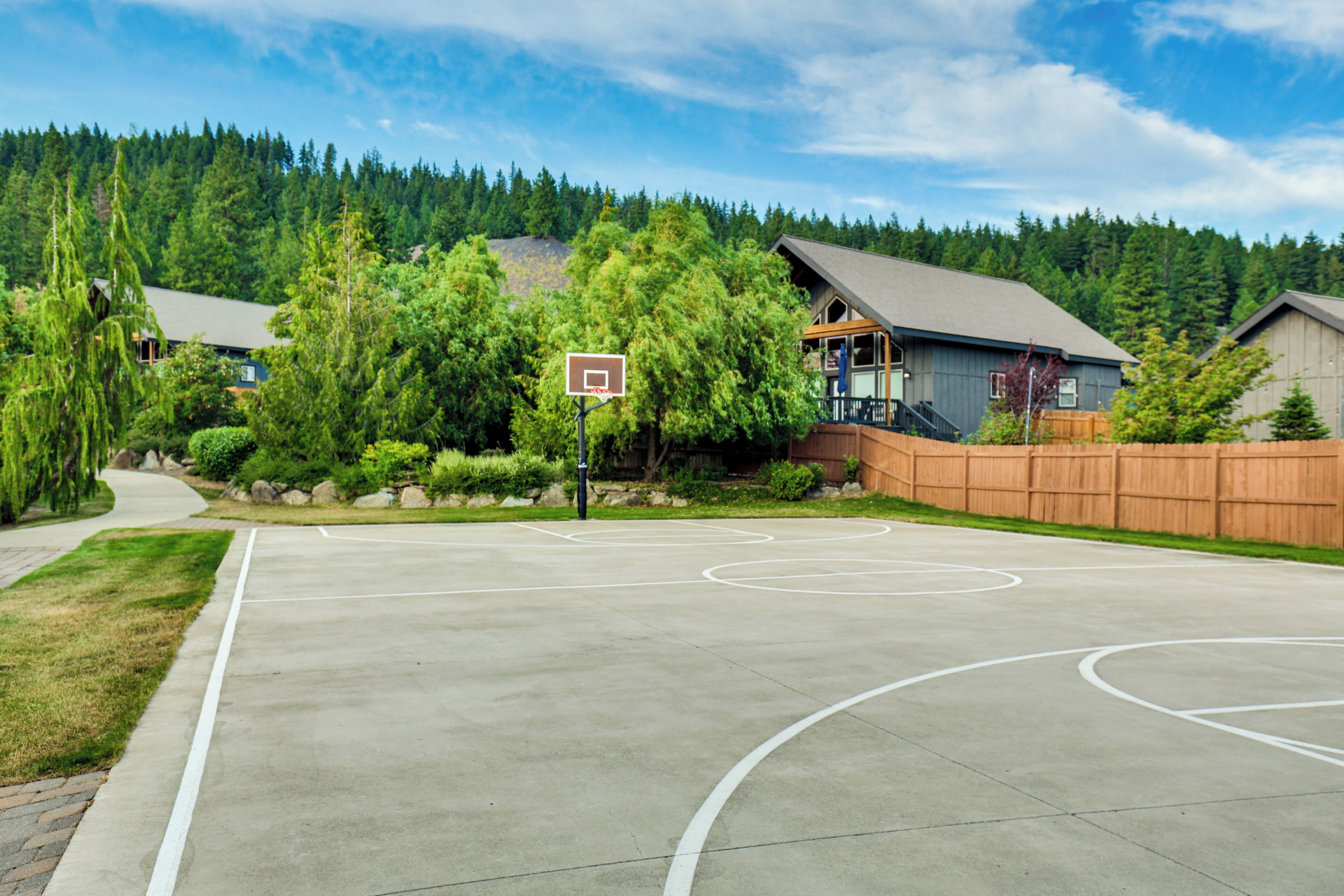 Una cancha de baloncesto con valla de madera, rodeada de árboles y casas.