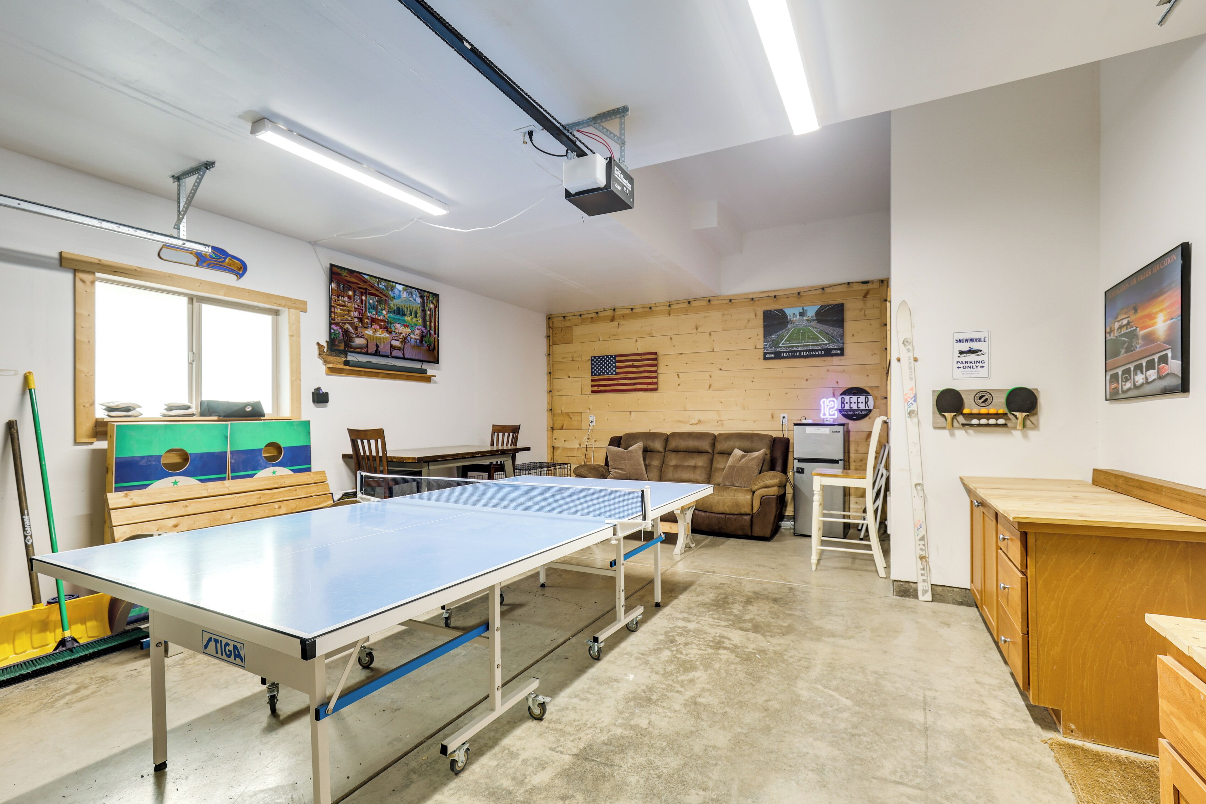 A room with a ping pong table, a wooden sofa, and a television mounted on the wall.